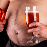 A man holds beer and smoked sausages against a large belly