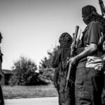 Black and white photo of police officers confronting three armed and masked men.